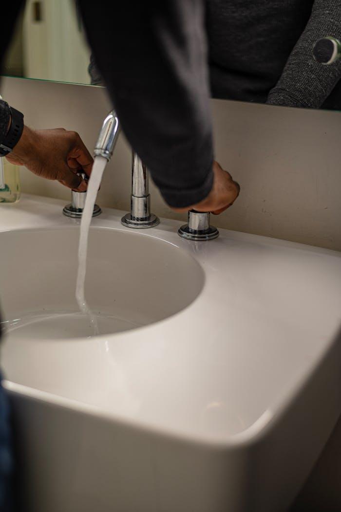 who-we-are Close-up of hands adjusting water flow in a modern ceramic sink with stainless faucet.